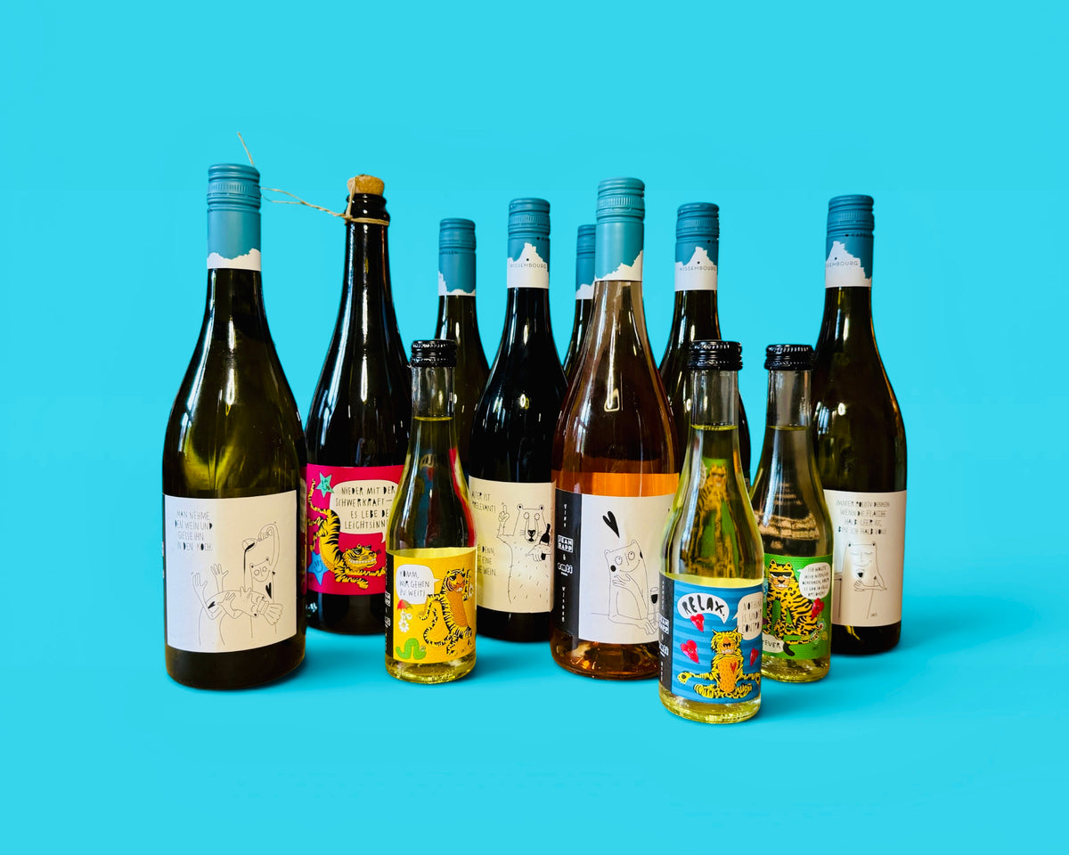 Zehn Weinflaschen mit Etiketten von EMTI für das Weingut Jean Rapp vor türkisem Grund: schwarz-weiße „Vino Wisdom“-Etiketten mit Bär und Strichfiguren, bunte „Spritz & Witz“-Etiketten mit Tigern, dazu eine Sektflasche mit Korken und kleine Flaschen