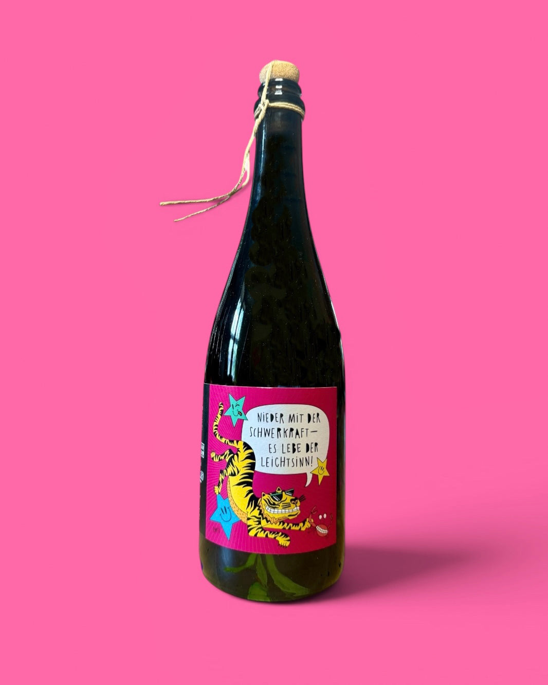Sektflasche mit Korken vor pinkem Grund, Etikett „Spritz & Witz“ von Jean Rapp und EMTI: ein Tiger mit Sonnenbrille fliegt zwischen Smiley-Sternen und einer Krabbe, Sprechblase „Nieder mit der Schwerkraft – es lebe der Leichtsinn!“