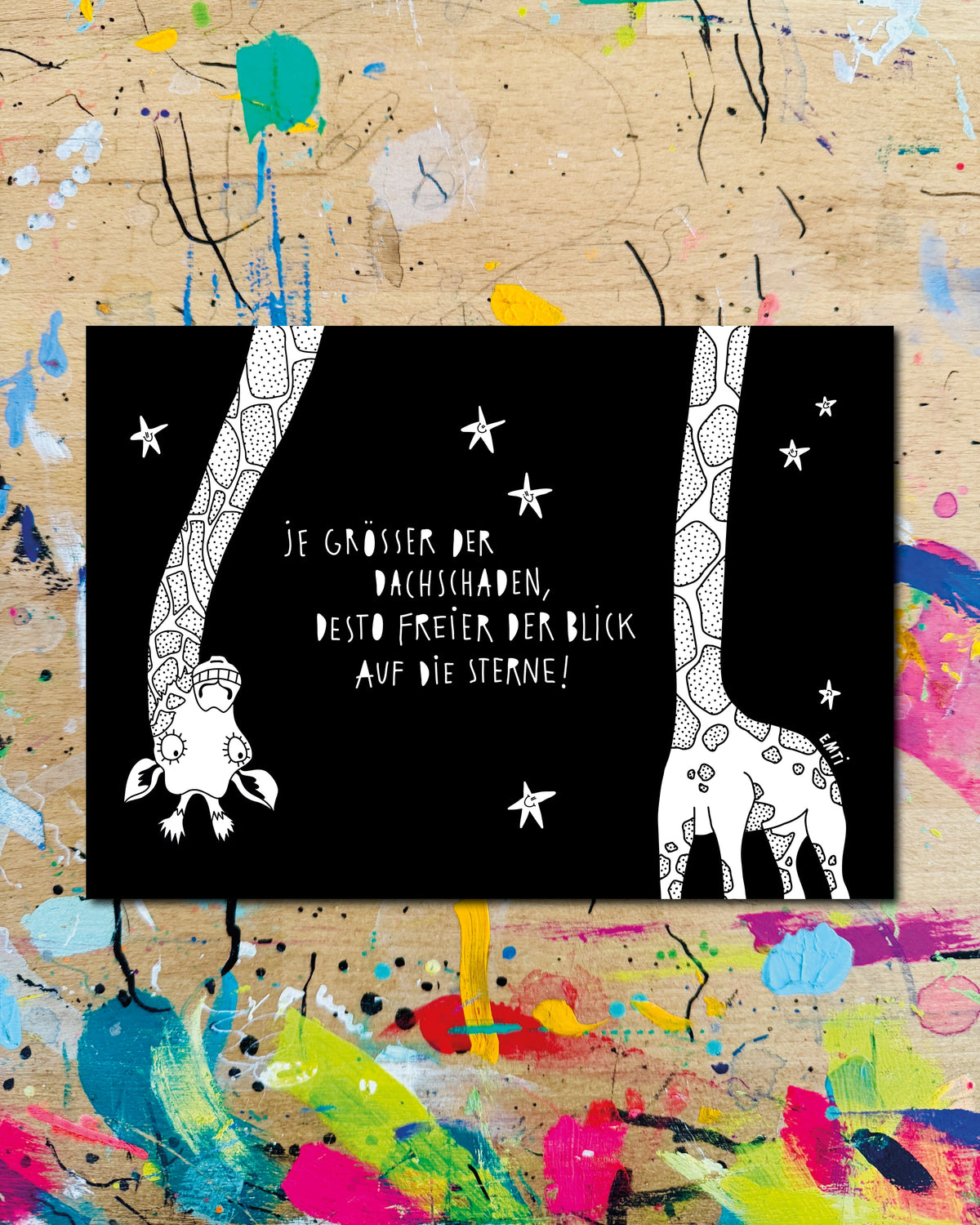 Postkarte quer: eine Giraffe lässt den Kopf zwischen Sternen herabhängen, auf schwarzem Grund, dazu der Schriftzug „Je größer der Dachschaden, desto freier der Blick auf die Sterne!“