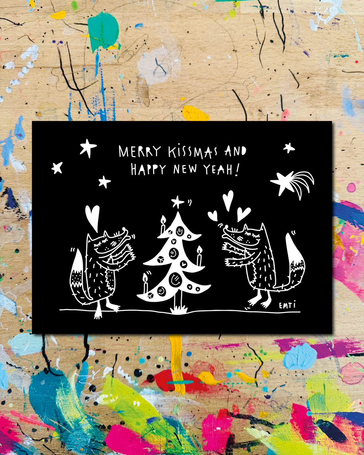 Postkarte quer: zwei Füchse mit Herzen neben einem geschmückten Tannenbaum auf schwarzem Grund, dazu der Schriftzug „Merry Kissmas and happy new yeah!“