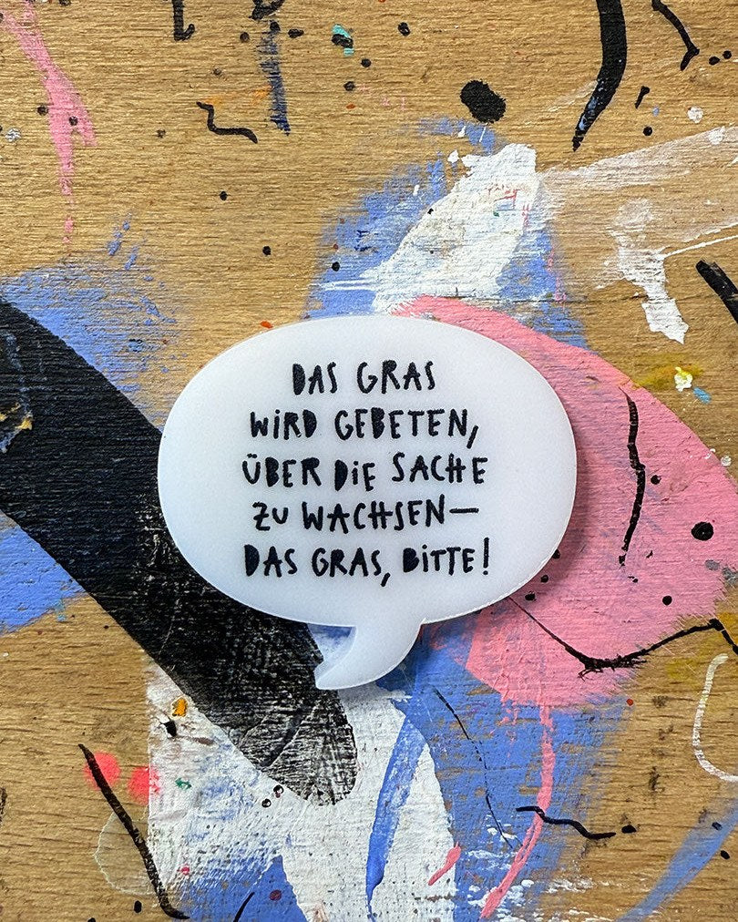 Sprechblase aus Acryl mit dem Schriftzug „Das Gras wird gebeten, über die Sache zu wachsen — das Gras, bitte!“