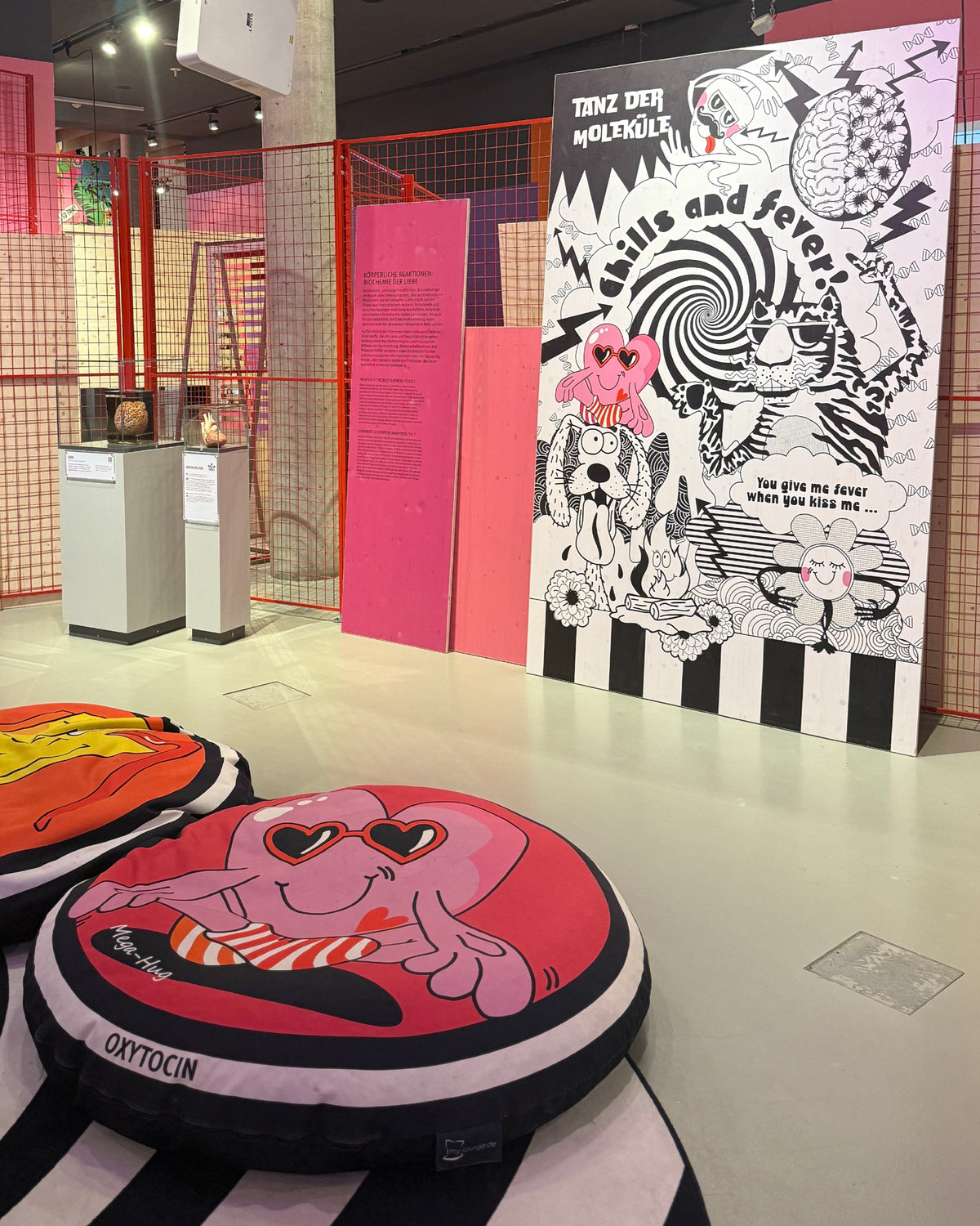 Schwarz-weiße Tafel „Tanz der Moleküle“ mit dem Schriftzug „chills and fever!“, davor ein rosa Sitzkissen mit einer Figur mit Herz-Sonnenbrille, beschriftet mit „Oxytocin“