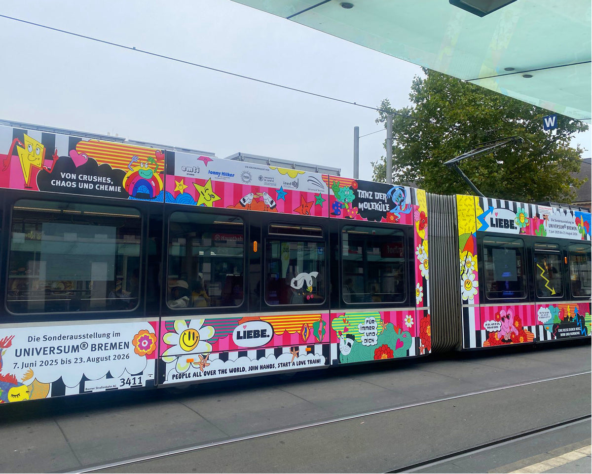 Die LOVETRAIN-Straßenbahn an einer Haltestelle mit den Schriftzügen „Von Crushes, Chaos und Chemie“, „Tanz der Moleküle“ und „Die Sonderausstellung im Universum® Bremen“